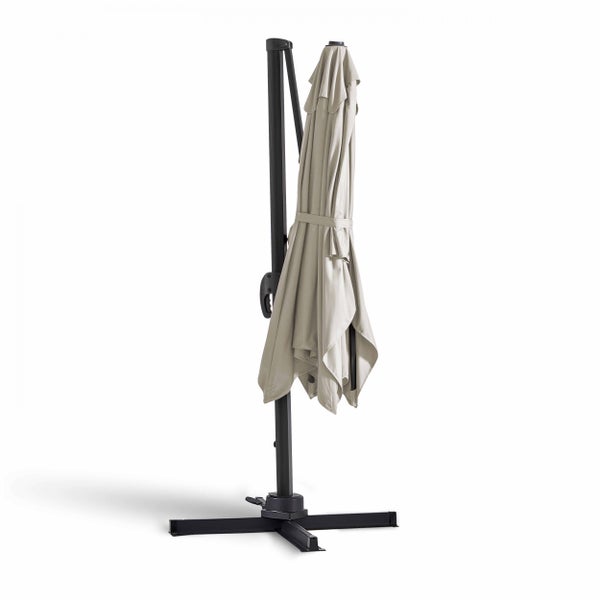 Geschlossener Ampelschirm mit dunklem Metallgestell und beigem Bezug auf einem Kreuzfuß.