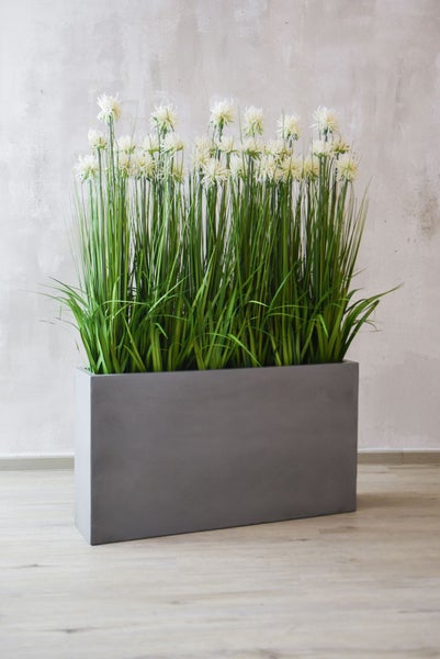 Grünes künstliches Gras in einem grauen quadratischen Topf mit Betonoberfläche.