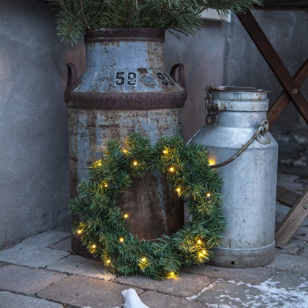 Dekorative Szene mit beleuchtetem Kranz und alten Milchkannen