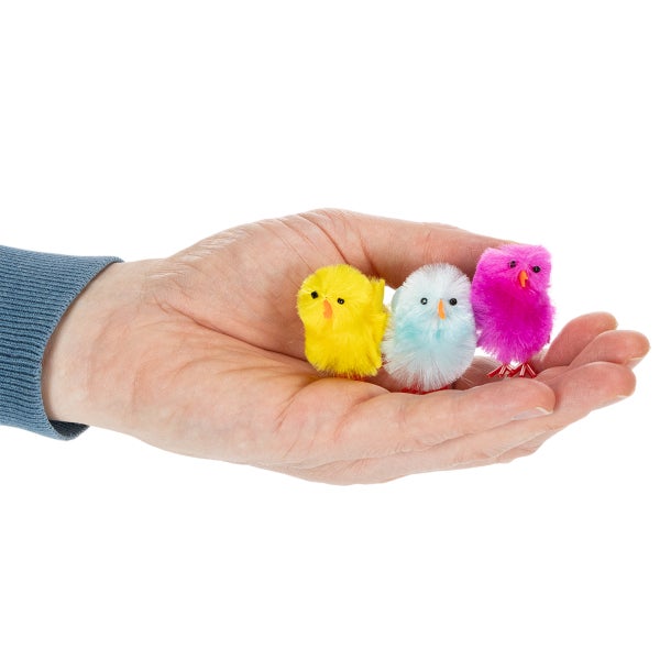 Drei kleine flauschige Dekoküken in Gelb, Blau und Pink auf einer Hand.
