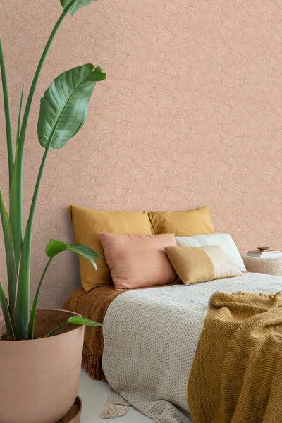 Schlafzimmer mit Vliestapete mit Ginkgo Muster, dekoriert mit Kissen, Tagesdecke und einer Zimmerpflanze in einem Tontopf.