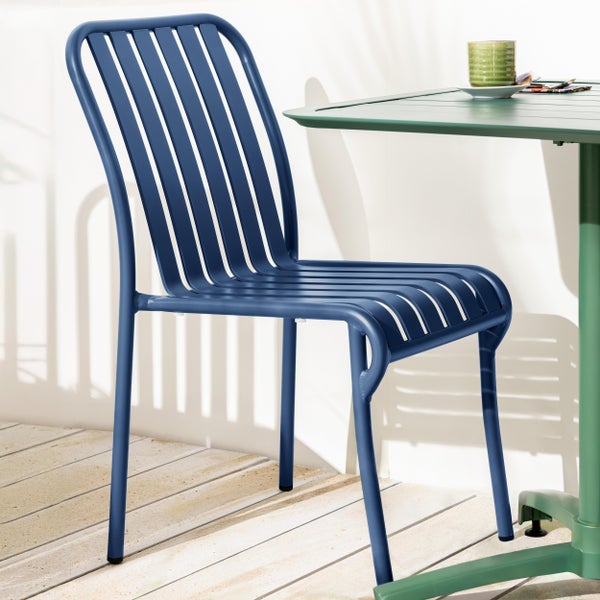 Blauer Gartenstuhl aus Metall mit vertikalem Lattendesign an einem Tisch auf einer hellen Holzterrasse.