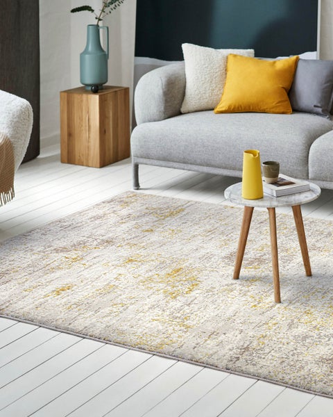 Moderner Kurzflorteppich mit abstraktem Muster in Grau und Gelb in einem hell eingerichteten Wohnzimmer vor einem Sofa.