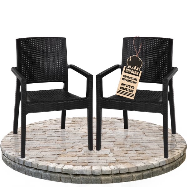 Zwei schwarze Rattanstühle mit Armlehnen stehen auf einem Steinsockel.