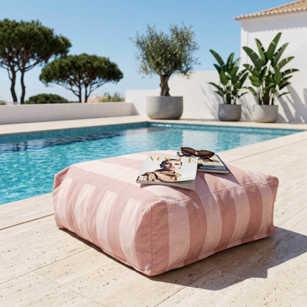Rosa gestreifter Outdoor-Sitzpouf auf einer hellen Terrasse am Pool mit Zeitschriften und Sonnenbrille.