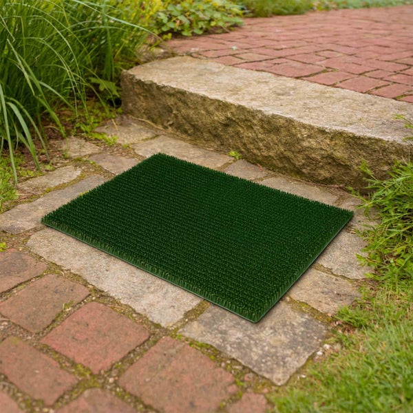Grüne Fußmatte aus Gummi auf einem Steinweg vor einem Hauseingang.