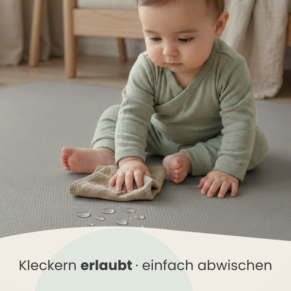 Baby auf einer strukturierten Spielmatte wischt Wassertropfen mit einem Tuch ab. Die Matte ist wasserabweisend und einfach zu reinigen.