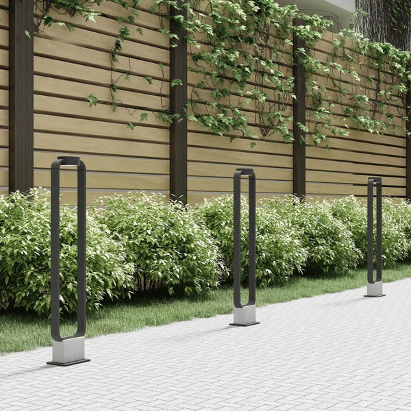 Drei moderne Außenleuchten in rechteckiger Rahmenform mit Betonfuß an einem gepflasterten Weg vor Hecke und Holzzaun.