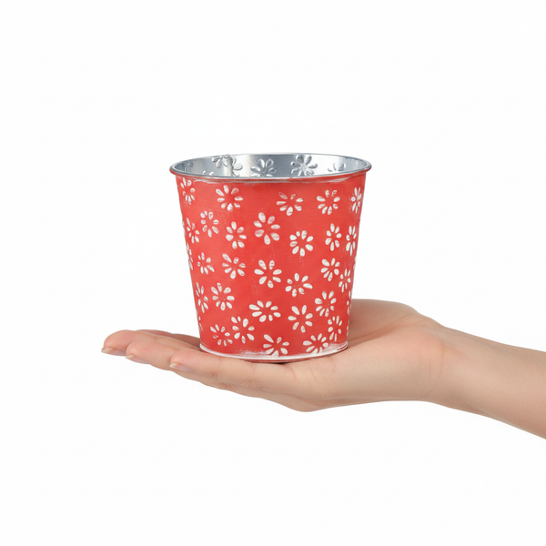 Kleiner runder Pflanztopf aus Metall in Rot mit weißem Blumenmuster, präsentiert in einer Hand.