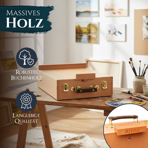 Ein Tischmalkoffer aus massivem Buchenholz von Artina auf einem Holztisch in einem hellen Atelier mit Malutensilien und Kunstwerken an der Wand.