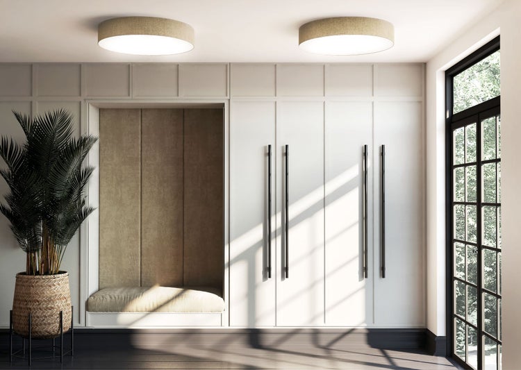 Moderner, heller Raum mit weißem Einbauschrank, schwarzen Griffen, gepolsterter Sitznische, zwei runden Deckenlampen und großer Palme im Korb.