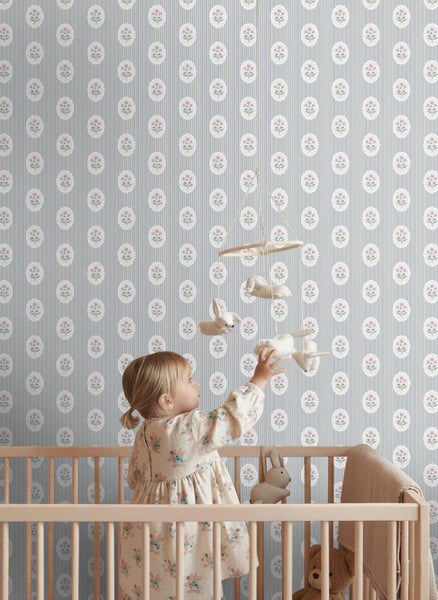 Vlies-Tapete mit Längsstreifen und floralen Medaillons an der Wand eines Kinderzimmers hinter einem hölzernen Gitterbett.