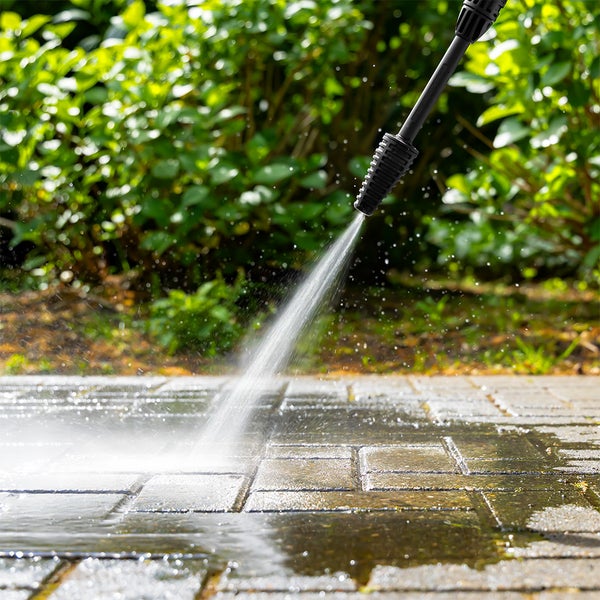 Hochdruckreiniger-Düse reinigt Pflastersteine mit einem starken Wasserstrahl im Garten vor Pflanzen.