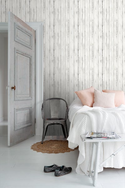 Helles Schlafzimmer mit Holzwandtapete, Bett und Stuhl.