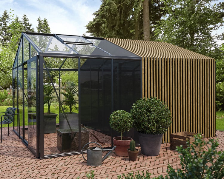 Modernes Gewächshaus mit schwarzem Aluminiumrahmen und Holzlamellen auf einer Ziegelterrasse mit Topfpflanzen.