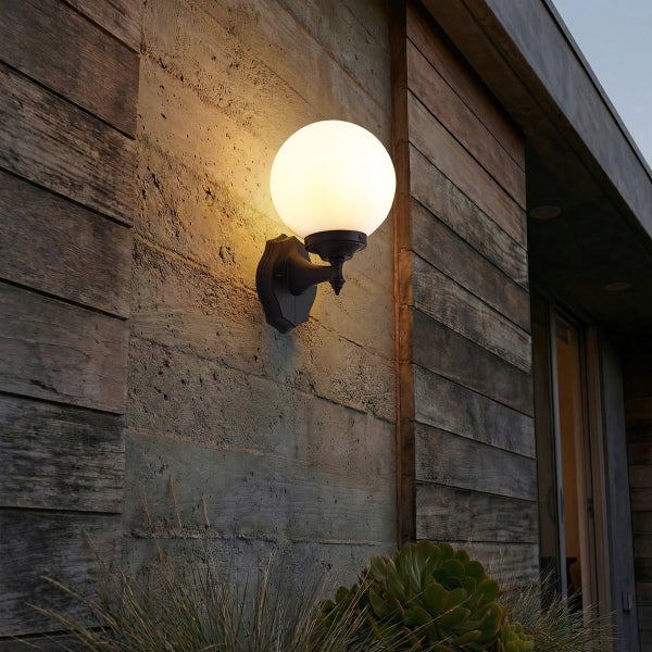 Kugelförmige Außenwandleuchte mit warmem Licht an einer strukturierten Wand.