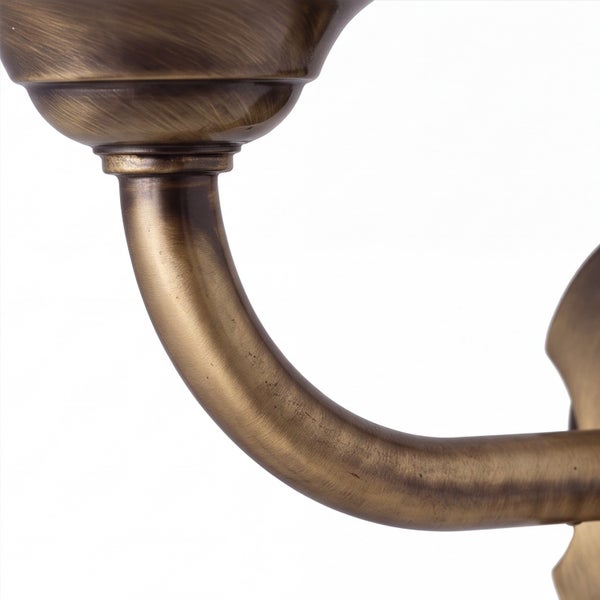 Detailaufnahme eines geschwungenen Lampenarms aus antikem Messing für eine Wandleuchte.