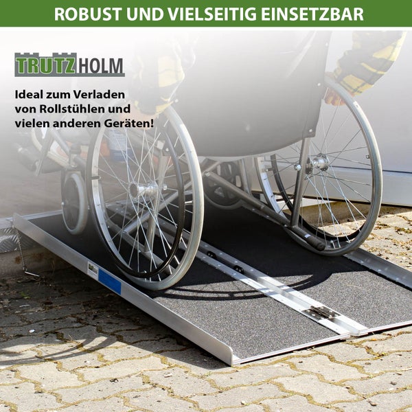 Klappbare Rollstuhlrampe aus Aluminium mit rutschfester Oberfläche, im Einsatz mit einem Rollstuhl auf hellem Boden, Trutzholm Logo.