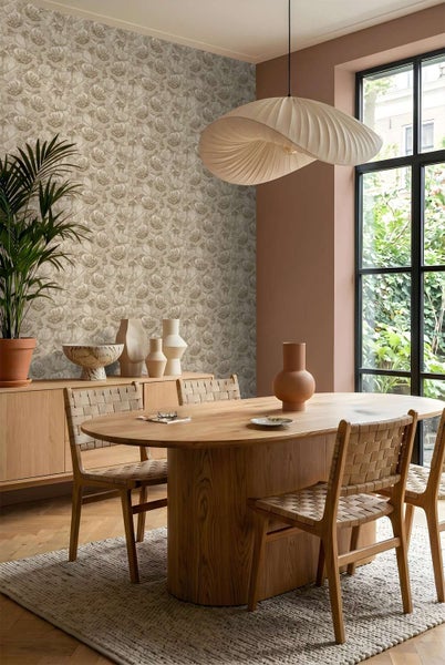 Esszimmer mit floraler Vliestapete, Holztisch, Stühlen mit Flechtoptik, Textilleuchte und Grünpflanze in modernem Wohnambiente.