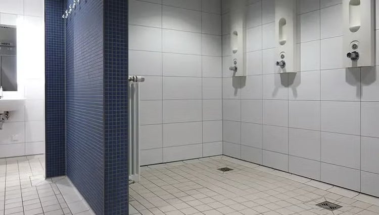 Moderne öffentliche Gemeinschaftsdusche mit weißen Fliesen, Wandarmaturen und Mosaikwand. Funktionale Sanitäranlage mit Bodenabläufen.