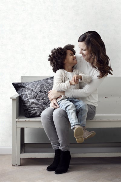 Eine Frau umarmt ein Kind auf einer Bank mit einem Kissen.