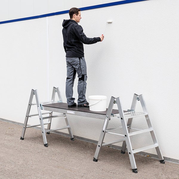 Mann streicht Wand von einer Arbeitsbühne aus