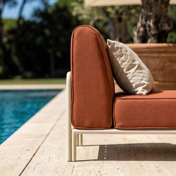 Detailansicht eines Gartensofas mit rostfarbenen Polstern und hellem Metallgestell am Poolrand.