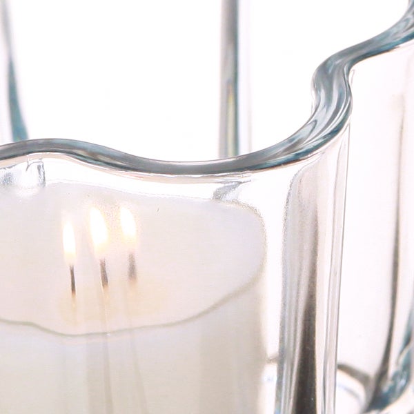 Weiße Kerze mit drei brennenden Dochten in einem gewellten Klarglas-Windlicht.