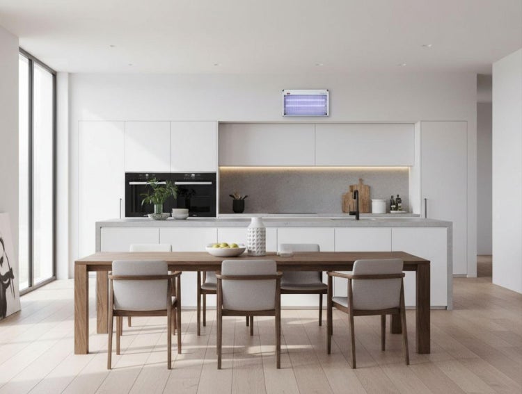 Elektrischer Insektenvernichter mit UV-Licht an der Wand einer modernen, hellen Küche mit weißer Küchenzeile und großem Holztisch mit vier Stühlen.