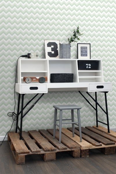 Dekorativer Schreibtisch mit Regalen, Schubladen und grauem Hocker auf einer Holzpalette