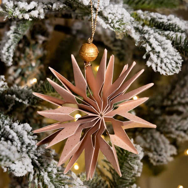 Weihnachtsanhänger in Sternform aus Papier hängend an einem verschneiten Tannenbaum