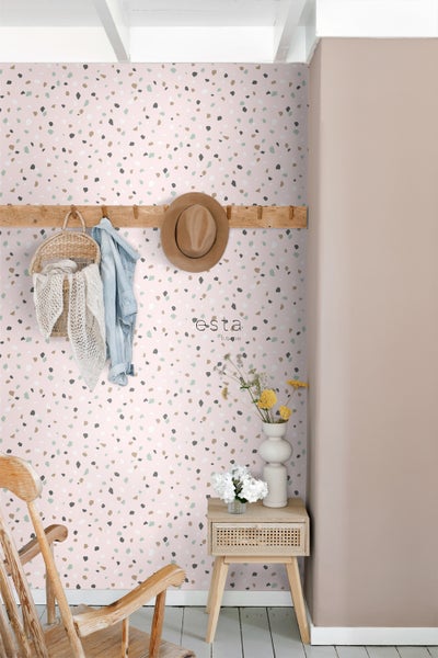 Dekoratives Zimmer mit Wand in Terrazzo Optik, Kleiderhakenleiste, Rattanhocker und Holzstuhl