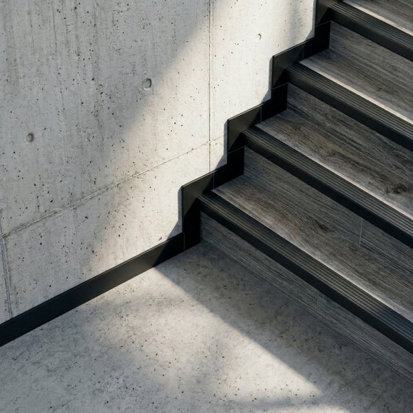 Moderne Treppe mit Fliesen in Holzoptik, schwarzen Treppenkantenprofilen und schwarzen Sockelleisten an einer Sichtbetonwand.