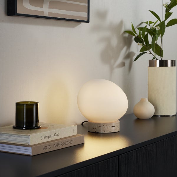 Moderne Tischleuchte mit eiförmigem Schirm aus mattem Glas und einem Steinfuß auf einem Sideboard mit warmer Beleuchtung.