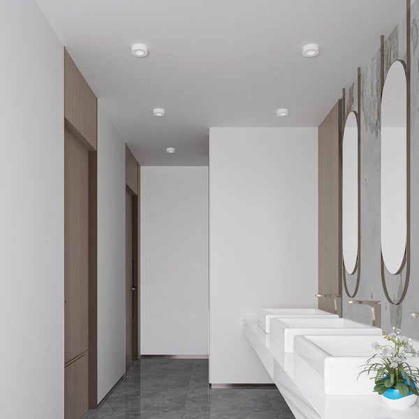 Modernes, helles Badezimmer mit drei weißen Aufsatzwaschbecken, hohen ovalen Spiegeln, Marmorboden und minimalistischen Einbaustrahlern.