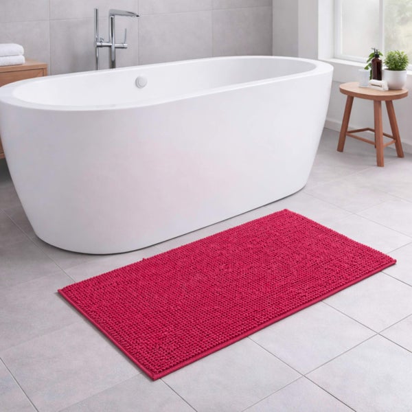 Pinke, strukturierte Badematte vor einer weißen, freistehenden Badewanne in einem modernen Badezimmer mit grauen Fliesen.