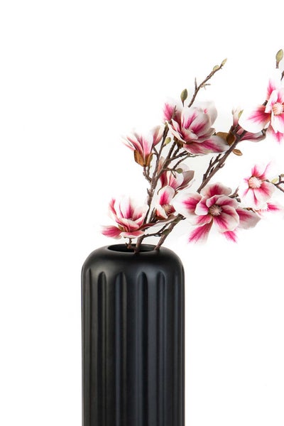 Künstlicher Magnolienzweig mit rosa-weißen Blüten in einer schwarzen geriffelten Vase.