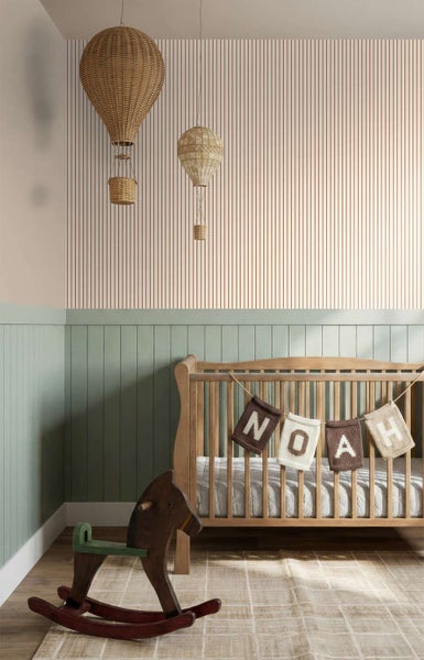 Kinderzimmer mit Holzgitterbett, Dekoration aus Heißluftballons an der Decke und einem Schaukelpferd auf dem Boden vor einer gestreiften Wand.