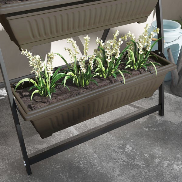 Vertikaler Pflanzkasten aus braunem Kunststoff in einem schwarzen Metallrahmen mit weißen Blumen auf einer Terrasse.