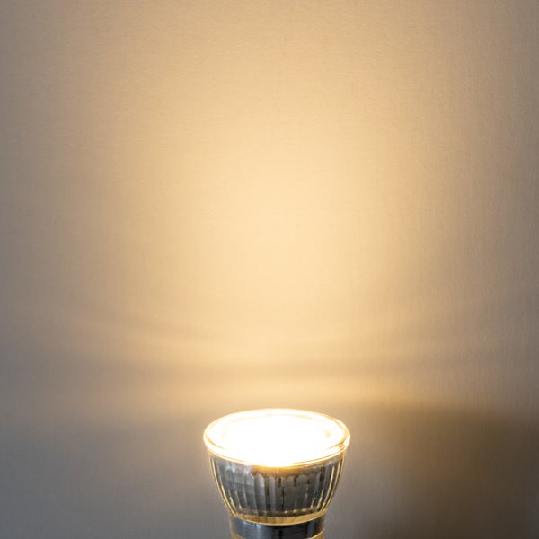 Leuchtendes LED-Leuchtmittel mit Reflektor, das warmweißes Licht an eine Wand wirft.