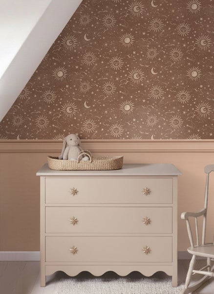 Kinderzimmer mit brauner Tapete mit Sonnenmuster, Mondmuster und Sternenmuster, Wandpaneelen, weißer Kommode mit Sternengriffen und Schaukelstuhl.