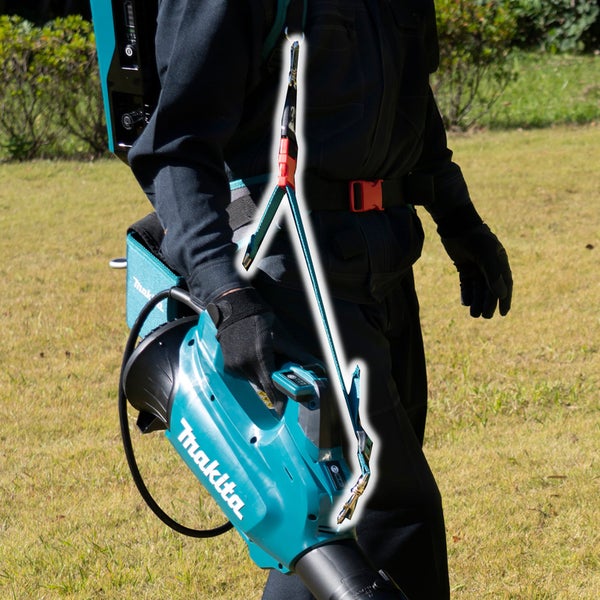 Person nutzt einen Makita Laubbläser mit einem Tragesystem im Garten, wobei die Befestigung am Schultergurt hervorgehoben ist.