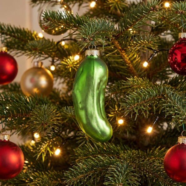 Weihnachtsbaumschmuck in Form einer Gewürzgurke aus Glas hängend an einem geschmückten Tannenbaum mit Lichterkette