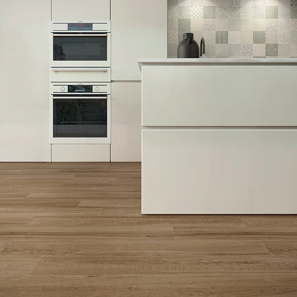 Moderne Küche mit Fliesenboden in Holzoptik, Einbaubackofen und heller Kücheninsel vor einer gemusterten Wandfliesenrückwand.