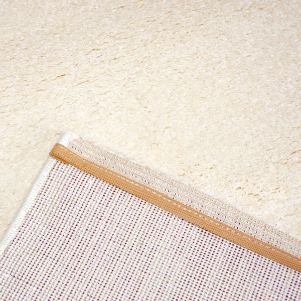 Nahaufnahme eines cremefarbenen Teppichs mit weichem Flor sowie der Unterseite mit Gewebestruktur und verstärkter Kante.