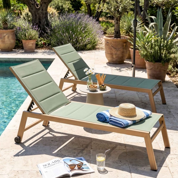 Zwei Gartenliegen am Pool mit Holzgestell und salbeigrüner Liegefläche, Beistelltisch, Handtüchern und mediterraner Bepflanzung im Hintergrund.