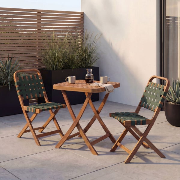 Ein Bistro-Set aus Holz auf einer modernen Terrasse, bestehend aus einem quadratischen Klapptisch und zwei Klappstühlen mit grüner Flechtung.