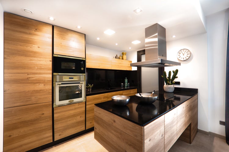 Moderne Einbauküche mit Holzfronten, schwarzer Arbeitsplatte, Kochinsel, Dunstabzugshaube und eingebautem Ofen mit Mikrowelle.
