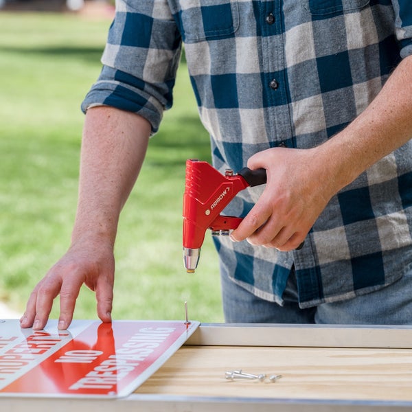 Eine Person befestigt mit einer roten Handnietzange ein Hinweisschild auf einem Metallrahmen.