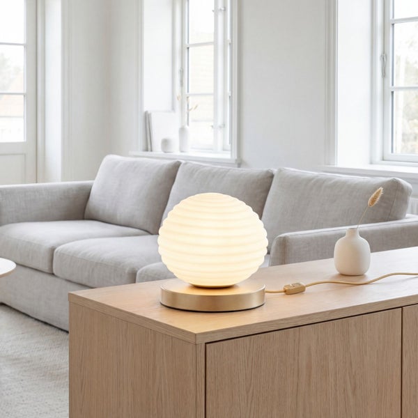 Moderne Tischleuchte mit geriffeltem Glasschirm und Metallfuß auf einem Sideboard aus Holz in einem hellen, minimalistischen Wohnzimmer.